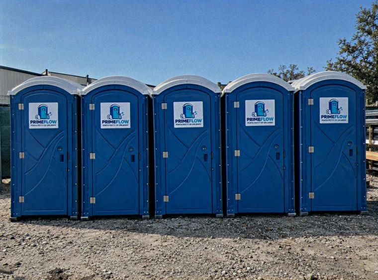 Row of blue portable restrooms lined up on a gravel work site