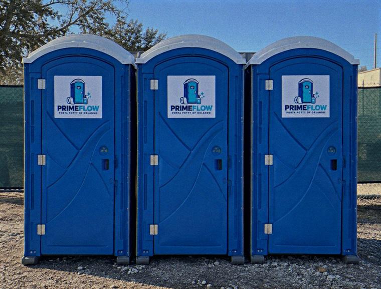 Three blue portable restrooms in a row against a green site fence